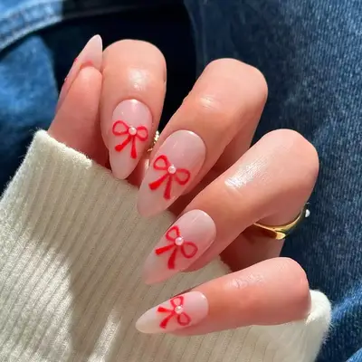 Pearl-dotted red bows on pearlescent nude nails