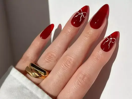 A red jelly manicure with subtle pink bows against a white wall