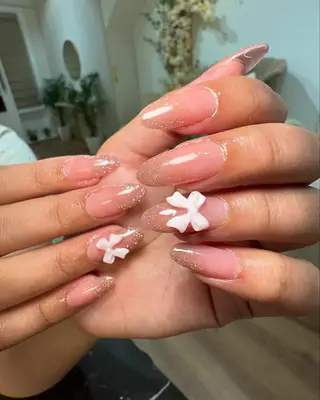 Shimmery almond nails with ombré glitter and bow appliqués 