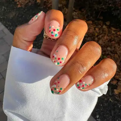 close up of hand showing off fresh manicure, bare base with red, white and green polka dots on top half of nails