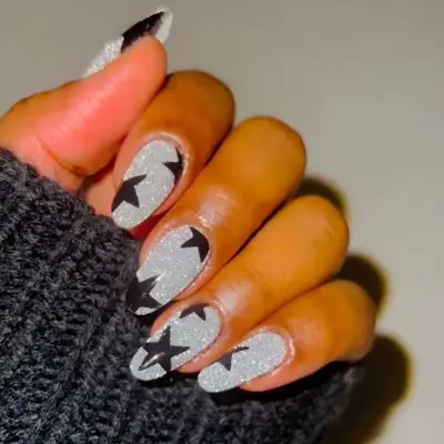 close up of hand showing off fresh manicure, silver nails with hand-painted black stars