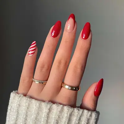 close up of hand showing off fresh manicure, one nail with red and white candy stripes, three nails plain red, one nail with red french tip