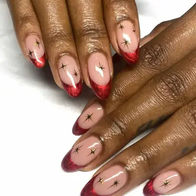 close up of hand showing off fresh manicure, sparkly red tips with bare base and hand-painted gold stars