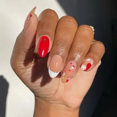 close up of hand showing off fresh manicure, christmas-inspired nails, one red nail with star, one french tip nail with silver line, one bare nail wit red polka dots, one nail with white snowflake and red accent
