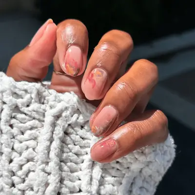 A hand with painted nails featuring ornamental designs, holding a textured white knitted fabric