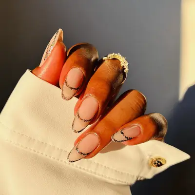 A well-manicured hand with detailed designed nails and a ring, partially covered by a white sleeve