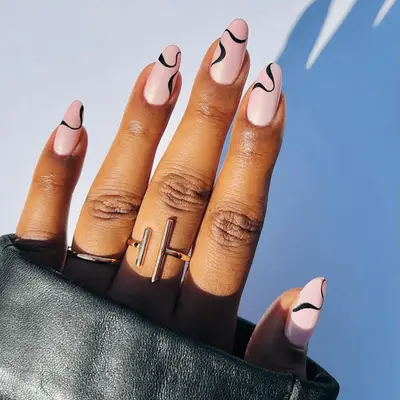 A hand with nail art featuring curved lines, wearing rings, and holding a leather garment