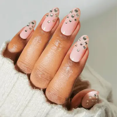 A hand with long nails featuring a pink base and rhinestone accents