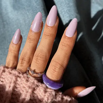 A hand with decorative long nails, accessorized with multiple rings, wearing a sweater sleeve