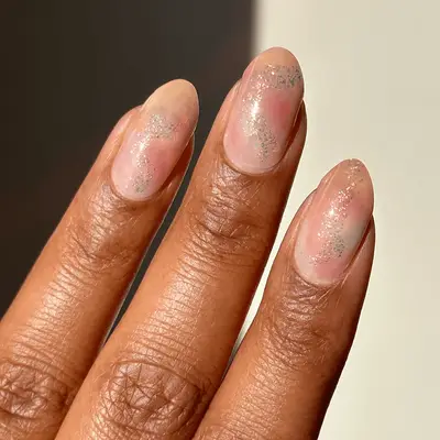 A hand with almond-shaped nails polished in a subtle shimmering finish