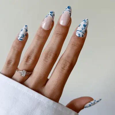 A hand with neatly manicured fingernails, featuring intricate blue floral designs