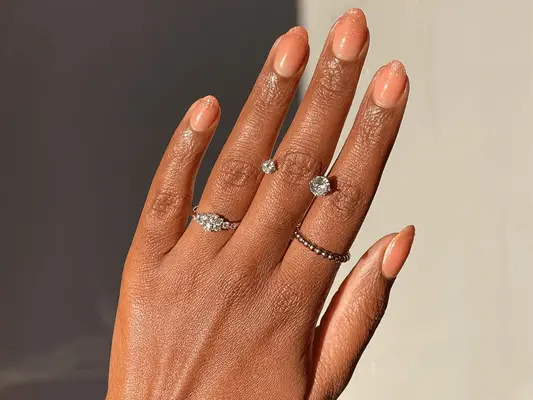 A hand decorated with rings and sporting neatly manicured nails, viewed in soft lighting