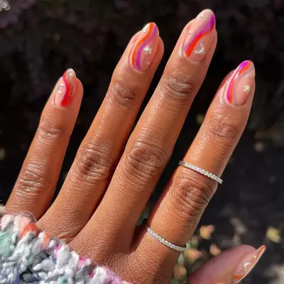 Pink and red swirl nails with a glossy nude base and silver stars and moons