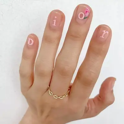 Pale pink Dior letters nail design with flower accent on clear background