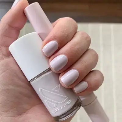 Ultra-pale pink nails holding Olive & June polish bottle