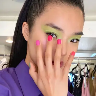 Model with green eyeshadow holds bright pink multi-toned manicure to face