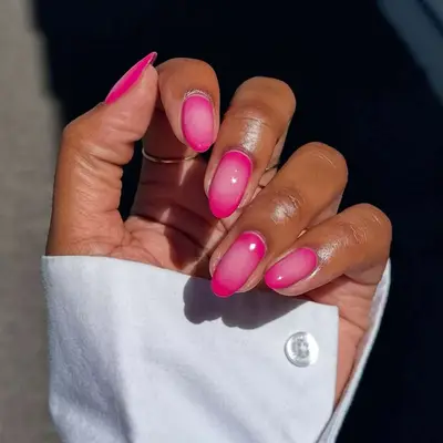 A hand with a well-manicured pink aura nail design
