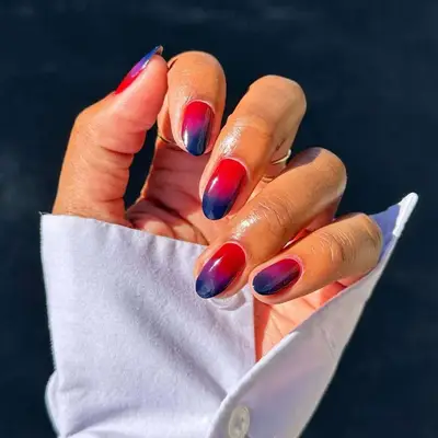 A close-up of painted fingernails in a gradient design, hand wearing a white shirt