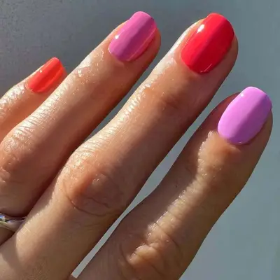 A close-up of manicure painted in different pink, red, and orange colors, against a neutral background