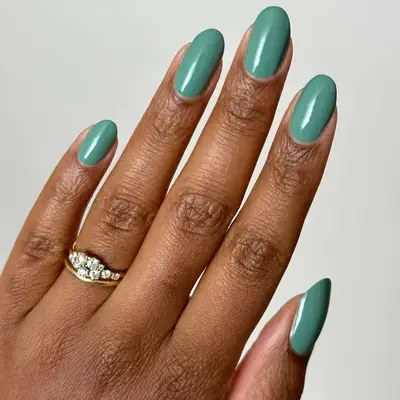 A hand wearing a ring with green styled nails