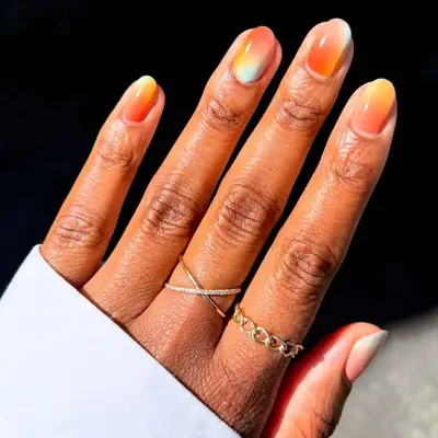 A hand with manicured sherbet-colored nails and gold rings on the fingers