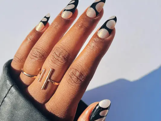 A hand with painted nails that have a black and sparkly white design