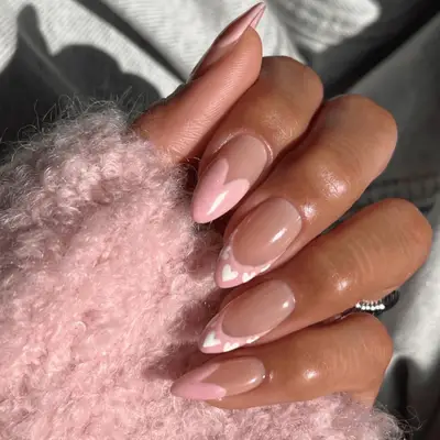 Almond-shaped acrylic French manicure with pink tips adorned with white hearts 