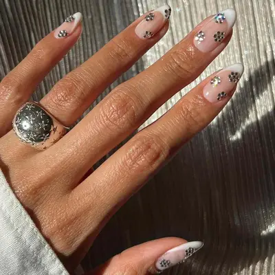 Close-up of manicure with neutral base, white French tips, and mirrored silver flower accents