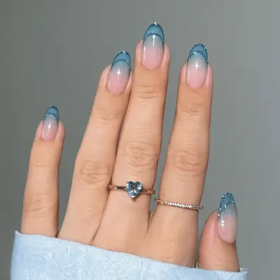 A close up of glittery double french tips in blue, with a blue ombre in the negative space.