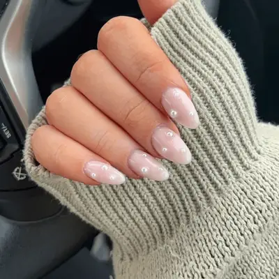 A close up of a white French ombre manicure with pearls