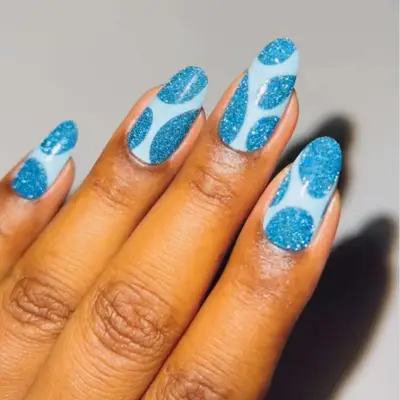 Manicure featuring a glittery blue design on oval-shaped nails