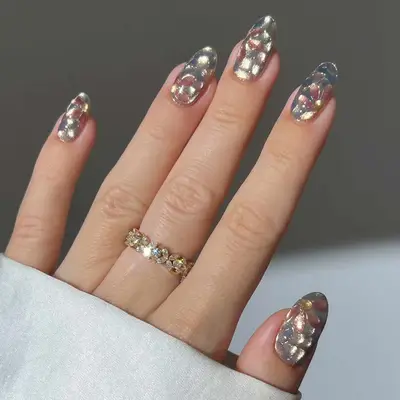 Hand with decorated floral glitter chrome nails and a gold floral ring