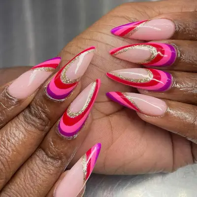 Manicured hands with stiletto nails in red, pink, purple, and gold glitter swirl pattern