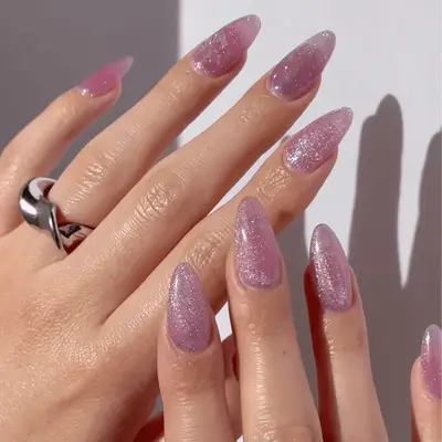 A close-up of a manicured hand with long nails and gold rings resting on denim