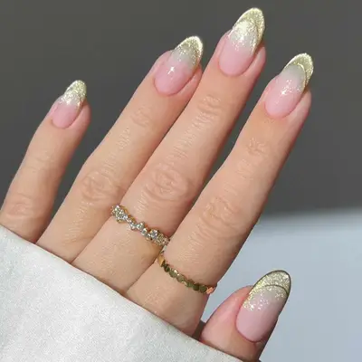 Manicured hand adorned with gold glitter nail tips and rings