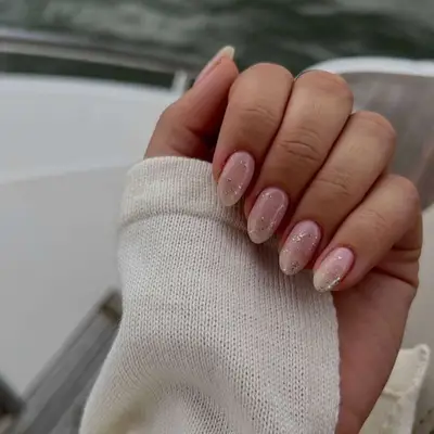 A hand with neatly manicured nails featuring a subtle gradient design, resting on a light sweater sleeve