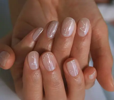 Short rounded nails with sheer nude base and white constellation design