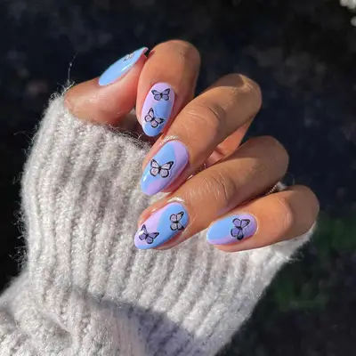 Manicure with purple and blue swirled base and butterfly emoji nail stickers