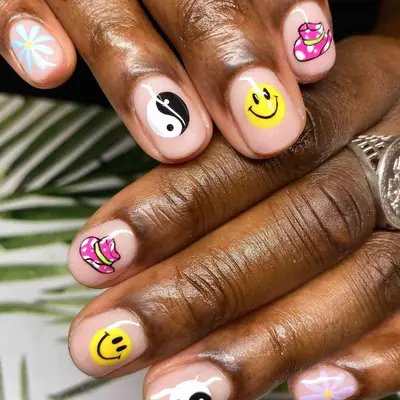 Neutral manicure with smiley face, yin/yang, cowboy hat, and flower emoji designs