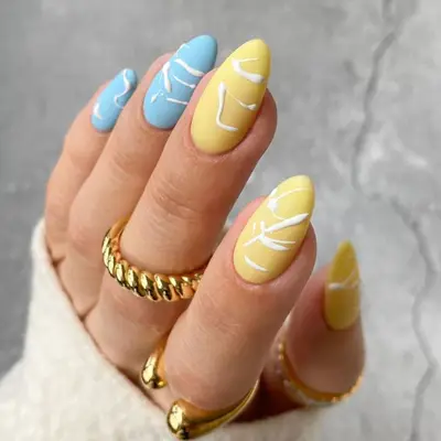 Two matte blue nails and three matte yellow nails with white splatter paint detailing.