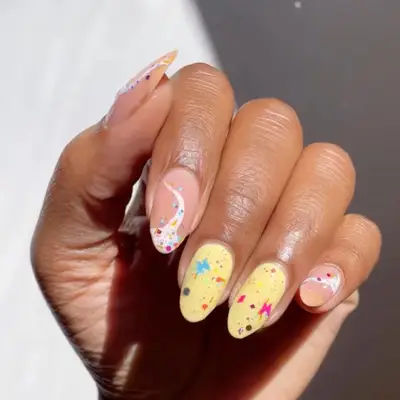 Yellow and nude nails with glow in the dark confetti glitter on top.