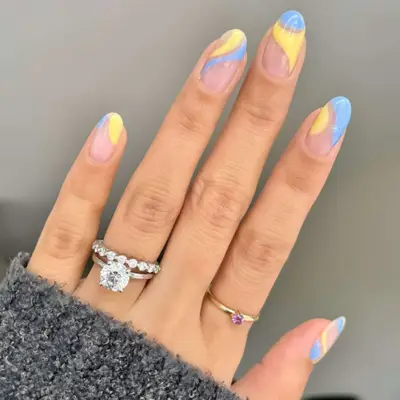 A nude manicure base with swirls of light blue and yellow.