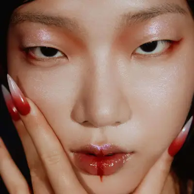 An Asian person with glittery makeup and red and white ombre stiletto nails - MYM Beauty Lunar New Year Nail Art Ideas