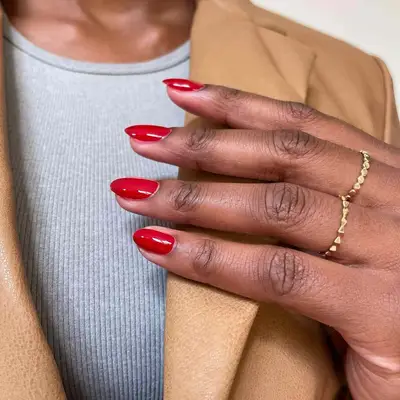 Close-up of red manicured hand with gold rings holding tan leather blazer lapel