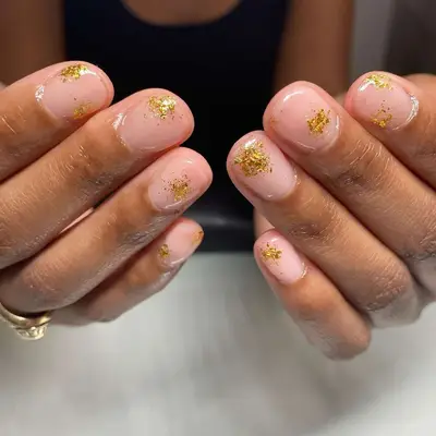 Close-up of short nails with neutral base and abstract gold foil designs