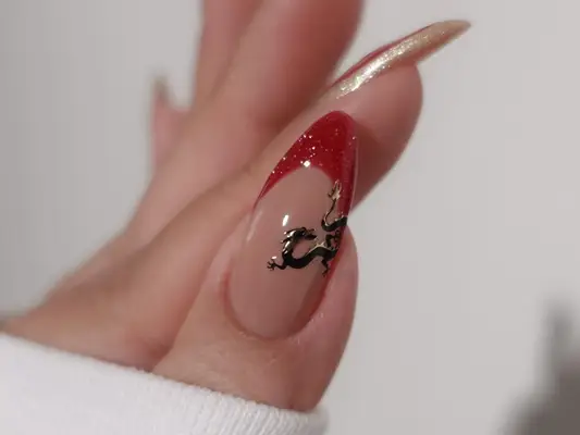 Close-up of manicure with red and gold glitter French tips and black dragon nail design