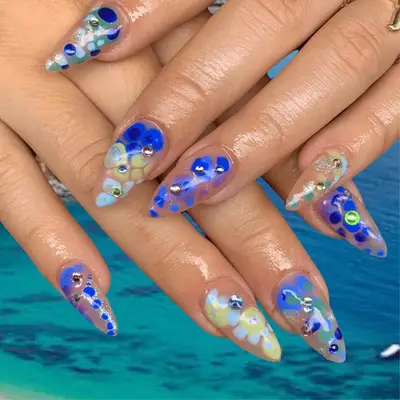 Oval nails with abstract blue, green, and purple dot designs and metallic gems.
