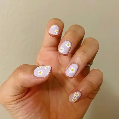 Short pastel pink nails with daisies dotted throughout