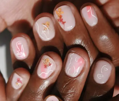 Short pink nails with pressed flowers and white line drawings of female body and faces