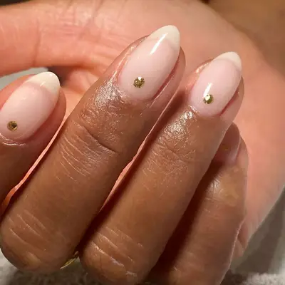 close up of pinky milky white nails with gold rhinestone on each one